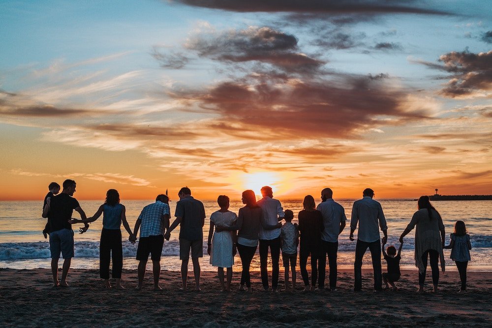 Family standing together on a beach at sunset holding hands
